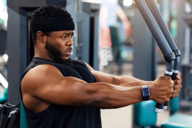 Konsantre siyah sporcu spor salonunda blok egzersizinde kas çalıştırıyor, yan görünüşte, fotokopi alanına bakıyor. Motive olmuş Afrikalı Amerikalı vücut geliştirici modern spor salonunda çalışıyor, Gaga güvertesi makinesi kullanıyor.