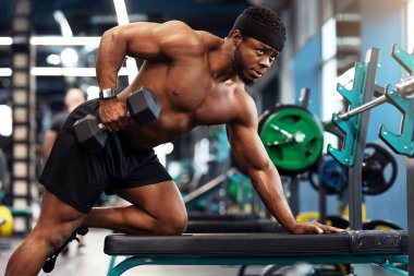 Seksi Afrikalı Amerikalı genç vücut geliştirici spor salonunda halter kaldırıyor, kolları üzerinde çalışıyor, fotokopi alanına bakıyor. Siyah, kaslı, üstsüz adam pazı egzersizi yapıyor. Sağlıklı yaşam tarzı kavramı