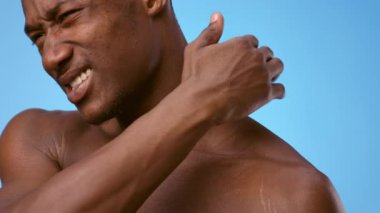 A young shirtless African American man showcasing pain in his neck against a vibrant blue background.