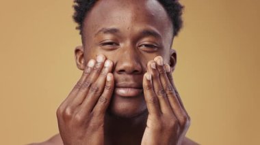 Genç bir Afrikalı Amerikalı adam sıcak ve tarafsız bir zemine yüz kremi sürüyor. Erkekler için cilt bakımı