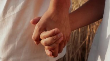 Çiftler gün batımında uzun altın otların olduğu geniş bir alanda el ele tutuşuyorlar. Sıcak ışık, aralarındaki yakın ilişkiyi güçlendirir..