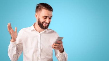 Sakallı adam akıllı telefon kullanıyor, internette sörf yapıyor mavi stüdyo üzerinden internet üzerinden iletişim kuruyor. Mobil cihaz kullanarak çalışan ya da uzaktan çalışan mutlu milenyum adamı