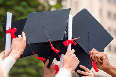 Öğrencilerin yetiştirdiği mezuniyet şapkaları ve diplomaları üniversite ya da üniversite binalarını devrediyor, yakın plan. Çok ırklı bir grup öğrenci, başlık ve diploma parşömenleriyle el kaldırıyor.