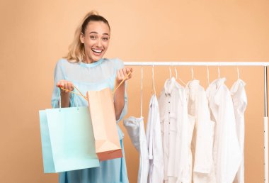 Satın Almaktan Mutluyum. Renkli alışveriş çantaları taşıyan neşeli genç bir kadının dikey portresi. Yeni kıyafetleri ya da hediyesi için heyecanlı. Ayakkabı ve elbiseleriyle korkulukların yanında duruyor.