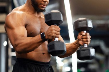 Ateşli siyah adam iki dambılla egzersiz yapıyor, kaslı pazıları üzerinde çalışıyor, fotokopi alanına bakıyor. Konsantre olmuş yakışıklı Afro-Amerikan üstsüz vücut geliştirici spor salonunda koltuk değnekleriyle sevişiyor.