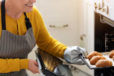 Gülümseyen yaşlı bir kadının evde pasta pişirmesi, lezzetli kruvasanları fırından çıkarması, fotokopi çekmesi. Önlüklü neşeli yaşlı bayan fırını açıyor, pastasını kontrol ediyor, mutfak içini kontrol ediyor.