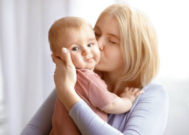 Sevgili anne, sarışın bir kadının, küçük bir çocuğu öptüğünün yakın plan portresi. Güzel bayan sevimli bebeğiyle bağ kuruyor, tatlı bir güneş ya da kız tutuyor ve öpüşüyor.