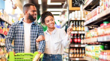 Neşeli Kara Eşler süpermarket koridorlarında bir araba dolusu ürünle marketten yiyecek seçiyor. Afro-Amerikalı Aile Dükkanda Birlikte Alışveriş Yapıyor