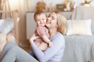 Sevgi dolu sarışın anne, evde küçük sevimli çocuğuyla bağ kuruyor. Oturma odasının içi, fotokopi odası. Mutlu genç bir kadın, gülen bebeğine sarılıyor, birlikte eğleniyor. Annelik kavramı