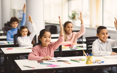 Okula geri dön. Çok kültürlü, küçük, mutlu ilkokul çocuklarından oluşan bir grup sınıfta sıralarında oturuyor, cevap için ellerini kaldırıyor, zevkle öğreniyorlar. Sosyal uzaklık