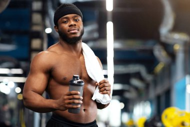 Antrenmandan sonra dinlen. Spor salonunda elinde su ya da protein içeceği ve havlu tutan Afro-Amerikan vücut geliştirici. Yakışıklı siyah kaslı adam modern spor salonunda egzersiz yaparken mola veriyor.