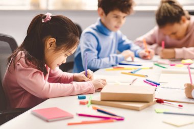İlkokulda ya da anaokulunda masada oturan küçük Asyalı bir kızın portresi renkli kalemlerle deftere çizilmiş. Kilitlendikten sonra tekrar açılıp okula dönmek.