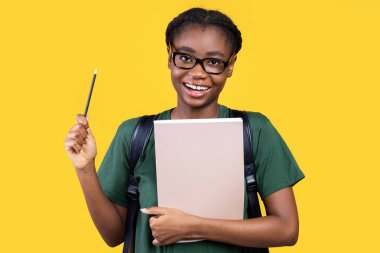 Bir fikrim var. Elinde kalem tutan, elinde kitaplarla ve arka plandaki kitaplarla kameraya gülümseyen yaratıcı Afrikalı kadın öğrenci. Eureka Anı