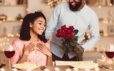 Sürpriz hazırlıyorum. Heyecanlı Afrikalı güzel Amerikalı kız arkadaşı, lüks bir restoranda ya da kafede romantik bir yemek sırasında elinde bir demet çiçek tutan mutlu erkek arkadaşından bir buket kırmızı gül alıyor.