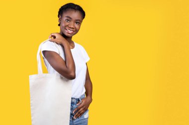 Beyaz Eko Torba Tutan Afro-Amerikalı Kadın Sarı Arkaplanda Poz Veriyor, Stüdyo Çekimi. Tekstil Alışverişi yapan Kadın Müşteri Pozu. Ekolojik Yaşam Tarzı ve Alışveriş