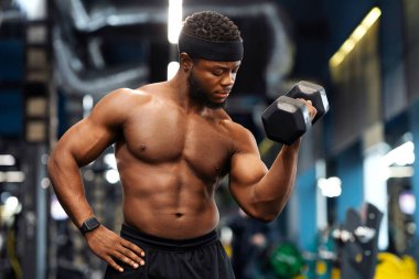 Pazı egzersizi. Yakışıklı Afro-Amerikan üstsüz sporcu modern spor salonunda dambılı eğitiyor, boş alan. Seksi siyah vücut geliştirici, tek eliyle halteri kaldırıyor.
