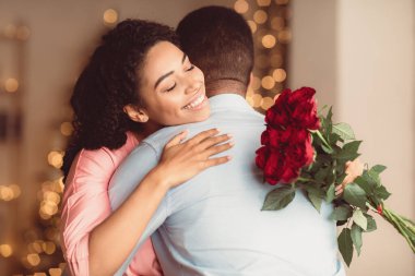Romantik İlişki. Gülümseyen Afrikalı Amerikalı kadının erkeğine sarılmasına ve elinde bir buket kırmızı gül tutmasına sevindim. Bir demet çiçekli kız arkadaşı erkek arkadaşını kucaklıyor, yıldönümünü kutluyor.