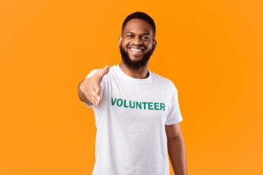 Neşeli gönüllü adam, sarı arka planda ayakta duran kameraya el sıkışmak için elini uzatıyor. Gönüllü İş, Gönüllü Takımımıza Katıl