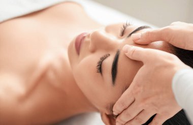 Spa terapisti, güzel Asyalı kadın için kafa masajı yapıyor, alnını ovuyor. Genç bayan güzellik salonunda gözleri kapalı bir şekilde uzanıyor, sağlık tedavisinden zevk alıyor, yakın plan çekimleri yapıyor.