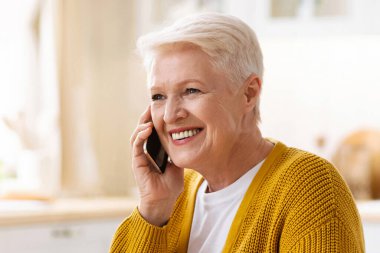 Neşeli büyükannenin evde yemek yerken telefonla araması, rahat bir mutfakta oturup boş bir yere bakması. Çekici son sınıf kadını telefonda konuşuyor, sağlıklı bir öğle yemeği yiyor.