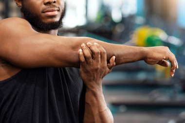 Isınma, esneme konsepti. Yakışıklı Afro-Amerikan sakallı sporcu antrenmandan önce kaslarını esnetiyor, spor salonunda vücut geliştirme eğitimi alan kaslı siyah adam fotokopi odasına bakıyor.