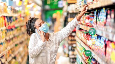 Siyah kadın telefonda konuşuyor, süpermarketten yiyecek alıyor. Cep telefonunda sohbet eden Afrikalı kadın markette market alışverişi yapıyor market arabalarıyla gıda ürünleri alıyor..
