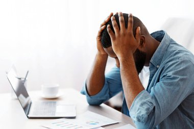 Siyahi girişimci masada oturuyor ve mali belgelere bakıyor, depresif Afrikalı Amerikalı iş adamı umutsuzluğa kapılmış, iş yerinde sorunlar yaşıyor, uzay kopyaları dolduruyor.