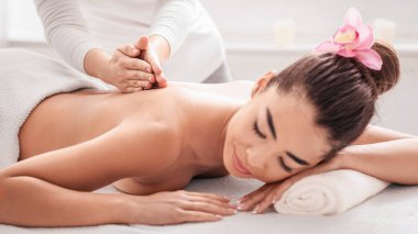 Güzellik ve Vücut Bakımı. Genç Asyalı kadın masaj terapisi sırasında Spa Salonu 'nda dinleniyor, profesyonel masör tarafından sağIık tedavisi görüyor, Masada uzanan sakin bir kadın,