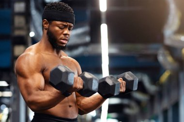 Yakışıklı Afro-Amerikan tişörtsüz vücut geliştirici spor salonunda koltuk değnekleriyle spor yapıyor, fotokopi çekiyor. Ateşli siyahi adam iki dambılla egzersiz yapıyor, kasları üzerinde çalışıyor.