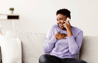 Erkek arkadaşınla ya da arkadaşınla güzel bir sohbet. Neşeli, genç, tombul, Afro-Amerikalı bir bayan akıllı telefonuna cevap veriyor ve arıyor, haberleri ya da dedikoduları duyuyor, evdeki oturma odasında kanepede oturuyor.