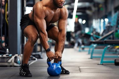 Spor salonunda kettlebell ile egzersiz yapan, fotokopi alanına bakan kaslı Afro-Amerikan vücut geliştirici. Atletik siyah adam ağırlık kaldırıyor ya da ağırlık kaldırıyor, vücut kasları üzerinde çalışıyor.
