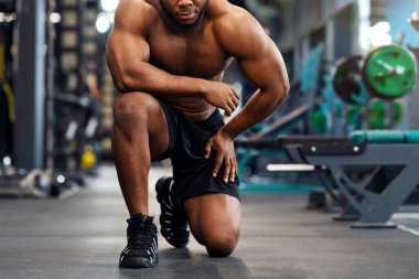 Modern jimnastik salonunda antrenman yaptıktan sonra yorgun Afrikalı Amerikalı üstsüz vücut geliştirici. Ciddi siyahi sporcu spor yaptıktan sonra dinleniyor, tek dizine yaslanıyor, boşluğu kopyalıyor.
