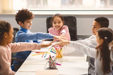 Gençlik Birliği Konsepti. Bir grup çok ırklı ilkokul öğrencisi masada toplanmış el ele tutuşarak eğleniyorlar. Dostluk ve kardeşlik, ortaklık ve destek