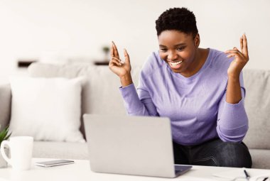 Virtual Communication. Happy black woman having online video conference with friends or family using computer, talking to web camera, gesturing, sitting on the couch in bedroom at home
