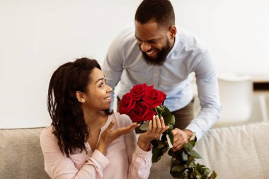 Sürpriz hazırlıyorum. Heyecanlı siyah kız arkadaşı elinde bir demet çiçek tutan ve onu Sevgililer Günü ya da Uluslararası Kadınlar Günü 'yle selamlayan mutlu erkek arkadaşından bir buket kırmızı gül alıyor.