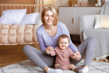 Güzel, beyaz bir anne bebek ellerini tutuyor, küçük çocuğuyla oynuyor, oturma odasında yerde oturuyor, fotokopi çekiyor. Anne ve bebek evde iyi vakit geçiriyorlar, birlikte oynuyorlar.