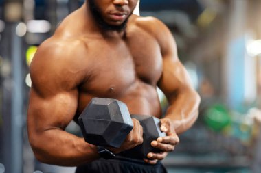 Spor konsepti için spor aletleri. Modern spor salonunda halterle egzersiz yapan siyah kaslı vücut geliştirici. Afrika kökenli Amerikalı atletik adam dambılla çalışıyor.