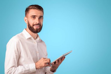 Formalite icabı giyimli bir adam online iş için tablet bilgisayar kullanıyor ya da mavi stüdyo arkaplanı üzerine çalışıyor. Kopya alanı olan panorama. Genç adam internetten iletişim kuruyor, video izliyor.