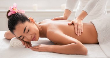 Salondaki profesyonel masörden spa tedavisi gören rahat Asyalı bir kadın sırt masajı yaptırıyor, gözleri kapalı masaya uzanıyor, Koreli bir kadın güzellik salonunda sağlık gününden hoşlanıyor, fotokopi çekiyor.