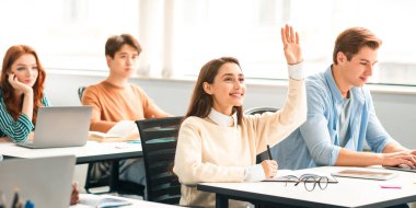 Eğitim Konsepti. Gülümseyen Bayan Öğrenci Elini Kaldırıyor ve Öğretim Görevlisine Bir Soru Soruyor, Not Defterine Yazıyor Üniversitede Ders Dinlerken. Sınıfta Öğrenen Çok Irklı Öğrenci Grubu