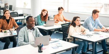 Ders Kavramı. İlgili çok kültürlü karışık ırk gruplarından oluşan bir grup öğrenci modern sınıfta bilgisayar başında oturmuş öğretmenlerini dinliyor, not defterlerine notlar yazıyor, çalışmak için geri dönüyorlar.