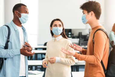 Gençlik ve Eğitim Konsepti. Çeşitli mutlu uluslararası sınıf arkadaşları konuşuyor, tek kullanımlık ameliyat maskeleri takan insanlar üniversitedeki konferans salonunda ayakta duruyor ve sohbet ediyorlar.
