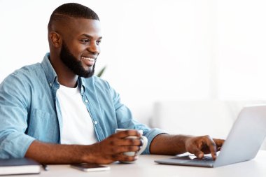 Bağımsız Kavram. Kahvesini yudumlayan ve bilgisayarında çalışan neşeli, siyah serbest çalışan, bilgisayarlı, uzaktan kumandayla eğlenen, uzay kopyalayan Afrikalı Amerikalı bir adam.