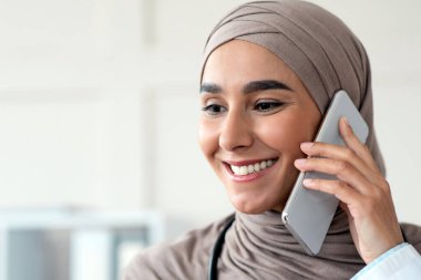 Cep telefonuyla konuşan ve fotokopi çekilen neşeli kadın müslüman kadın portresi. Sırıtkan tesettürlü genç bayan akıllı telefondan hastayla konuşuyor.