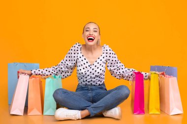 Butik 'te. Heyecanlı Kız Pastel Yellow Stüdyo Duvarı 'na izole edilmiş renkli alışveriş torbalarıyla oturuyor, Boşluğu Kopyala