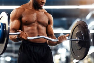 Spor salonunda, fotokopi alanında ağır halterle egzersiz yapan kaslı Afrikalı Amerikalı vücut geliştiriciye yakın çekim. Atletik siyah adam ağırlık kaldırıyor ya da ağırlık kaldırıyor, kollar ve göğüs kasları üzerinde çalışıyor.