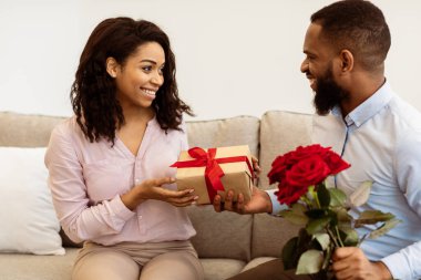 Özel bir olayı kutluyoruz. Gülümseyen Afrikalı Amerikalı adamın portresi kız arkadaşına hediye paketi ve bir buket kırmızı gül veriyor. Uluslararası Kadınlar Günü 'nde bayanı selamlayan mutlu adam.