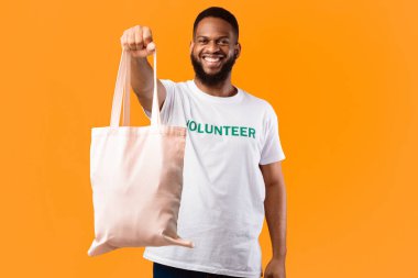 Plastik kullanmayı bırak. Afrikalı Gönüllü Adam Beyaz Çevre Çantası Gösteriyor Kamera Pozisyonu Sarı Stüdyo Arkaplanında Duruyor. Tüketim ve Ekoloji, Plastiksiz Yaşam Tarzı