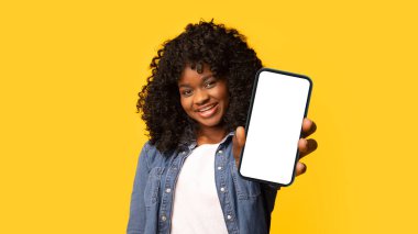 Neşeli genç siyahi kadın sarı stüdyo arka planındaki kameraya baş parmağını gösteriyor, kopyalama alanı. Şirin Afro-Amerikan bayan jest yapıyor, bir şeyler öneriyor,