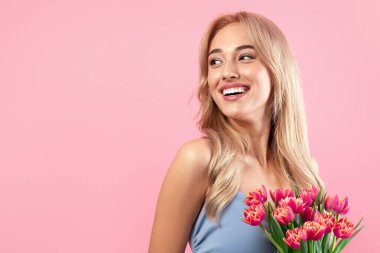 Kadın Günü konsepti. Pembe stüdyo arka planında bahar tatilini kutlayan taze lalelerle çekici genç bayan. Güzel milenyum sarışını elinde bir buket çiçekle